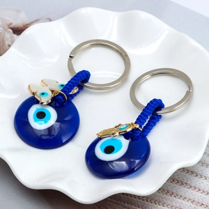 Golden evil eye keychain with blue glass hamsa hand and butterfly charms on white plate