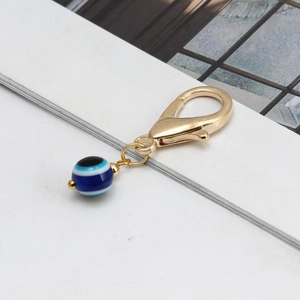Détail du fermoir mousqueton doré et perle œil bleu sur un accessoire de porte-clés