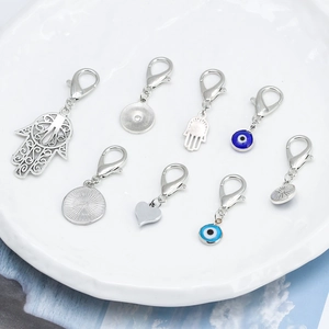 Detail of silver Hamsa Hand and Evil Eye pendants with lobster clasps on ceramic plate