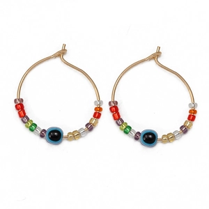 Detail of gold hoop earrings with colorful glass seed beads and evil eye charm