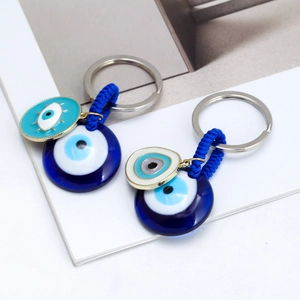 Blue evil eye keychain with glass pendant and woven cord on a white artistic background