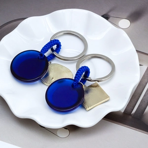 Evil Eye keychain with blue woven cord and golden pendant in white ceramic tray