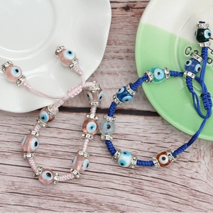 Handmade evil eye charm bracelets with adjustable pink and blue woven cords on ceramic