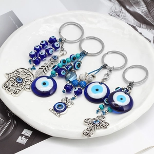 Artistic Evil Eye and Hamsa hand keychains with blue beads on a ceramic tray