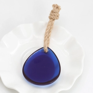 Detail of blue teardrop glass pendant with off-white hemp rope on white ceramic plate