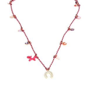 Macro detail of bohemian braided necklace featuring horseshoe and red balloon dog charms