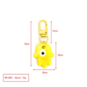 Vista macro del llavero Hamsa amarillo con ojo turco y dimensiones del producto