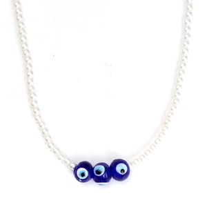 Close-up of white faux pearl necklace featuring three blue evil eye charms on white background