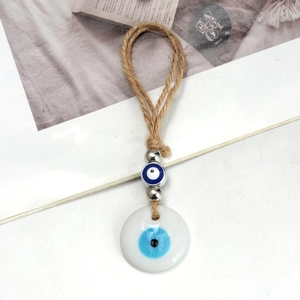 Macro detail of Evil Eye pendant with braided jute rope and blue glass beads on white desk