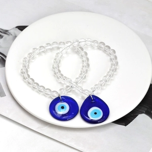 Macro view of evil eye beaded bracelets with blue teardrop pendants on white ceramic tray