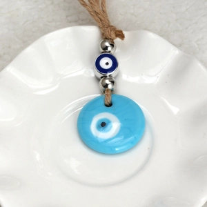 Handcrafted blue evil eye keychain with hemp rope and metal beads on ceramic dish