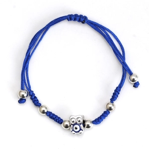 Macro detail of blue braided cord bracelet with silver owl evil eye charm and metal beads