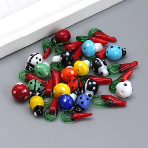 Detailed view of colorful lampwork glass charms in mushroom ladybug and chili shapes for DIY