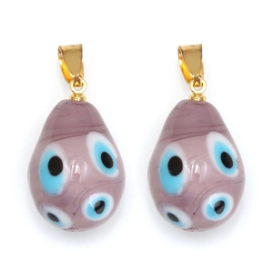 Détail de pendentifs gouttes en verre lilas avec motifs œil bleu et attaches dorées