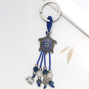 Detail of evil eye turtle keychain with blue tassels, hamsa hand and elephant charms