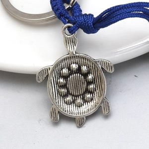 Detailed close-up of a vintage silver turtle keychain with a blue woven rope strap