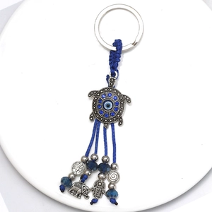 Detail of blue evil eye turtle keychain with hamsa hand, elephant charms and blue tassels