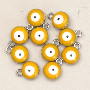 Macro detail of nine yellow enamel evil eye charms for DIY necklace making on fabric