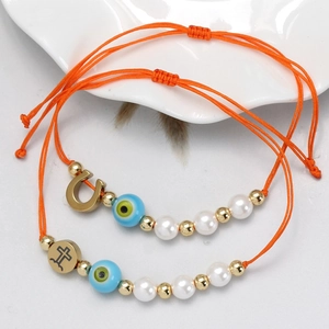 Detail von roten Evil-Eye-Armbändern mit Kunstperlen und Goldanhängern auf Weißteller