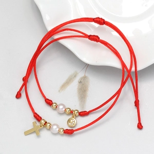 Detail von roten geflochtenen Armbändern mit goldenem Kreuz, Mond und Perlenperlen