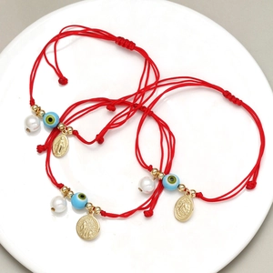 Detailaufnahme roter gewebter Armbänder mit Evil Eye Perlen und religiösen Anhängern
