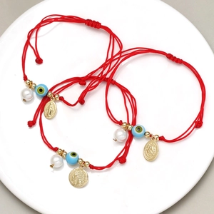 Detail von roten Kordelarmbändern mit bösem Blick, Perle und goldener Heiligenmedaille