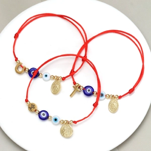 Rote geflochtene Evil-Eye-Armbänder mit goldenen Hufeisen- und Kreuzanhängern auf Tablett