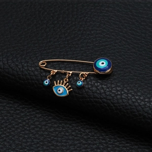 Detail der goldenen Anstecknadel mit blauen Evil Eye Anhängern auf schwarzem Lederhintergrund