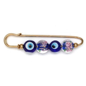 Macro shot of gold-tone pin brooch with evil eye and floral glass beads on white background
