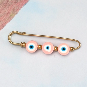 Macro shot of gold safety pin brooch with three pink evil eye beads and gold spacers