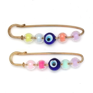 Close-up of golden safety pins featuring a blue evil eye bead and colorful faceted stones