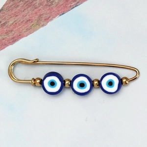Macro shot of gold Evil Eye safety pin brooch with blue beads on grey textured background
