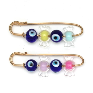 Detail showing two golden safety pins with blue evil eye beads and candy charms