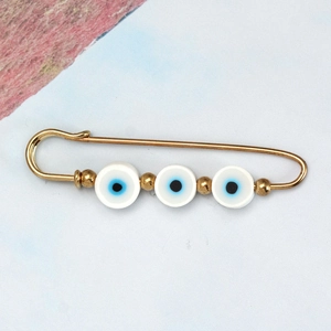Detailed close-up of golden evil eye safety pin brooch with three blue and white beads