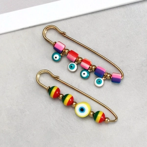 Macro detail of gold safety pins with colorful polymer clay evil eye beads and charms