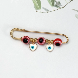 Detail van gouden veiligheidsspeld broche met evil eye kralen en witte hart hangers