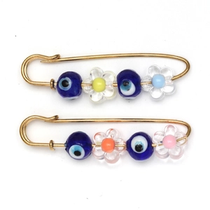 Detailed macro view of two gold safety pin brooches featuring blue evil eye beads and floral accents
