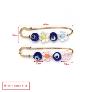 Detail view of gold-plated safety pins with blue evil eye beads and colorful resin flower charms