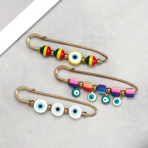 Detail view of gold safety pins with colorful clay beads and evil eye charms