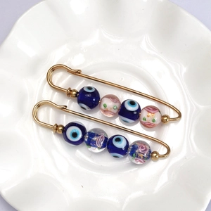 Golden Evil Eye safety pins with crystal beads and floral glass charms on a white plate