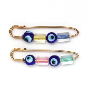 Macro detail of gold safety pin brooches with Turkish Evil Eye beads and colorful resin blocks