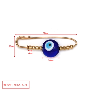 Detailed view of evil eye safety pin brooch with golden alloy and blue bead accents