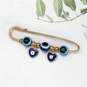 Detailweergave van een gouden veiligheidsspeld broche met blauwe boze oog kralen en hartjes