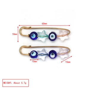 Detail view of gold safety pins featuring blue evil eye beads and colorful star charms