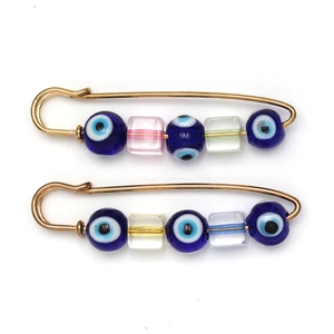 Detail of golden safety pin brooches featuring blue evil eye beads and striped square glass