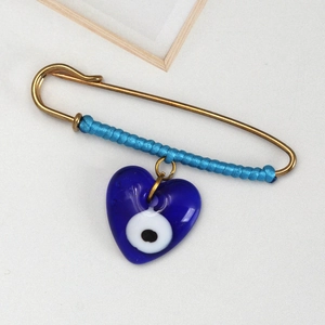 Detail of blue braided rope on gold safety pin with heart-shaped Evil Eye glass pendant
