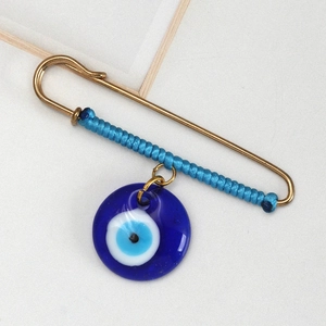 Detailed macro view of the light gold safety pin with blue woven cord and Evil Eye charm