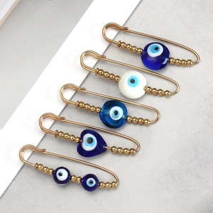 Set of five gold Evil Eye safety pins with blue and white beads on stone background