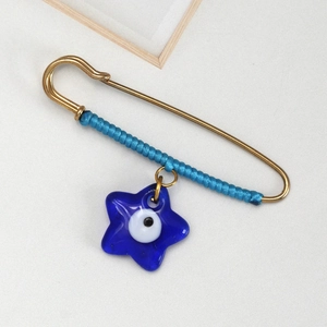 Detail of gold safety pin brooch featuring blue woven cord and evil eye star charm