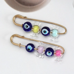 Detailed view of two gold evil eye safety pins with colorful candy-shaped beads